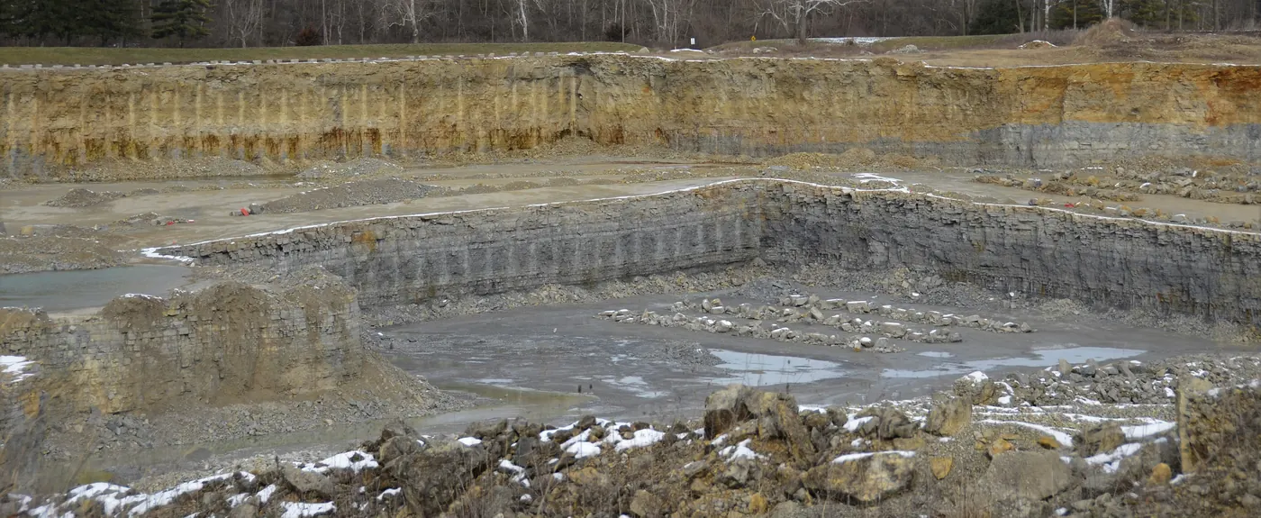 Quarry wall showing bands of pale rock and darker gray rock under a layer of soil
