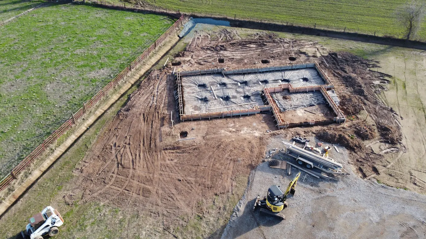 Aerial view of wooden forms and plastic sheeting laid out for a new house slab, with round holes drilled in the ground