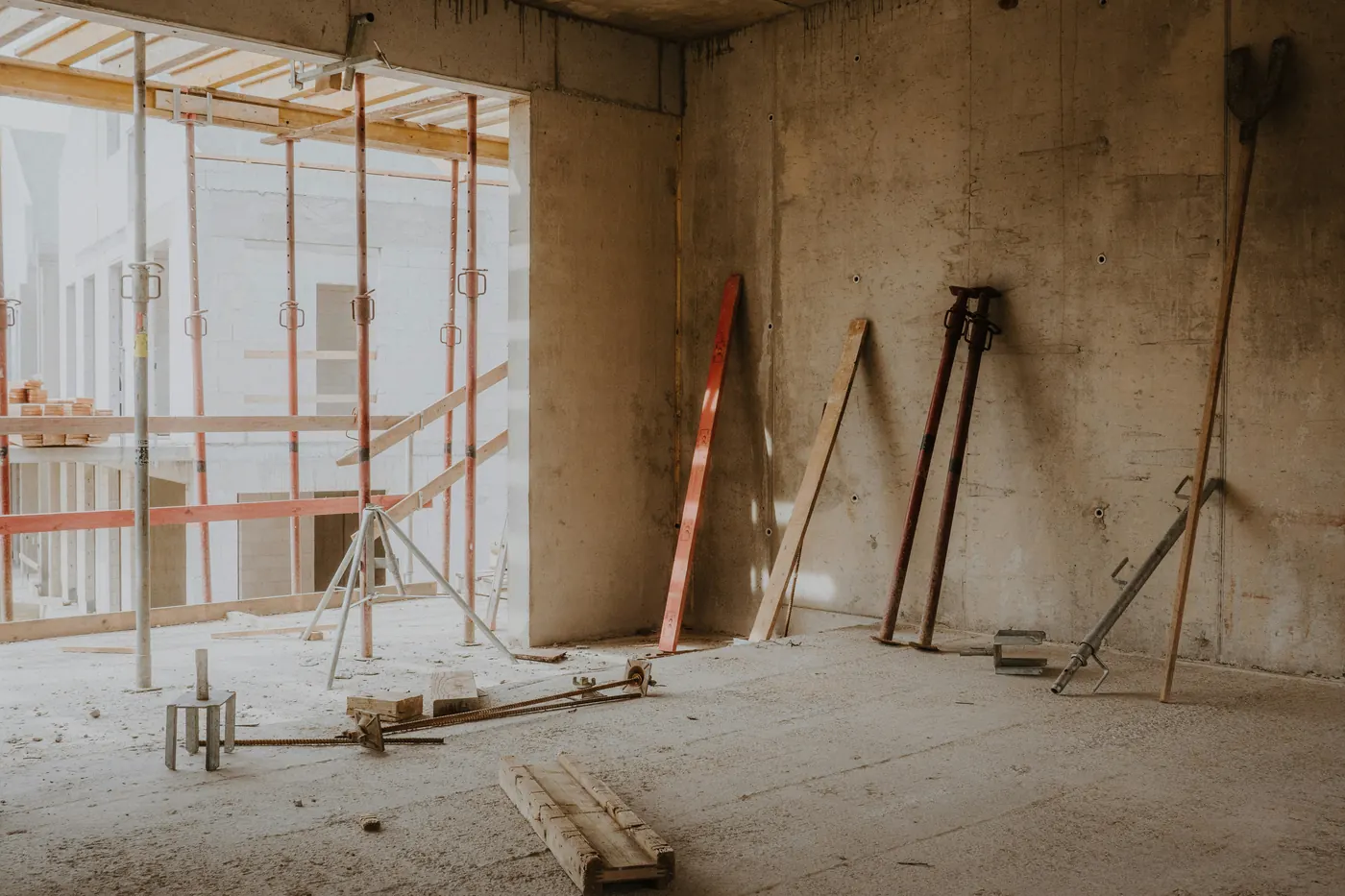 Adjustable steel props and timber leaning against a bare concrete wall inside a building under construction
